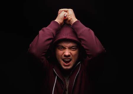 Crazy drug addict with a drug syringe, portrait of young adult person under the influence of drugs on a black background.の写真素材