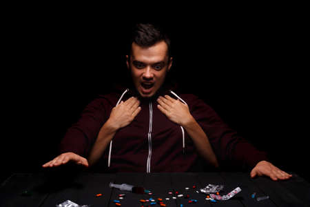A guy looking at different drugs. Womans hands holding a man from the back on a black background. Drug abuse concept.の写真素材