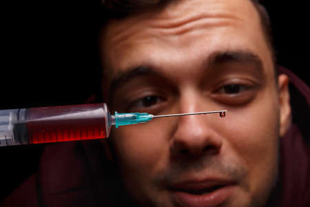 Macro picture of a druggy face and a syringe on a black background. A boy looks closely at a syringe with drugs and smiles.の写真素材