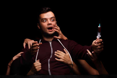 Womans hands holding an addict away from drug syringe. Freak with needle on a black background. Drug obsession concept.の写真素材