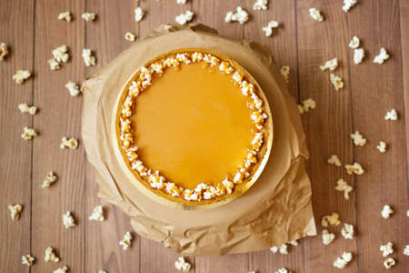 Close-up of a round cake with condensed milk, honey and a shortbread decorated with sweet popcorn on a paper stand and on a blurred wooden background. Sweet and tasty dessert with popcorn, top view.の写真素材