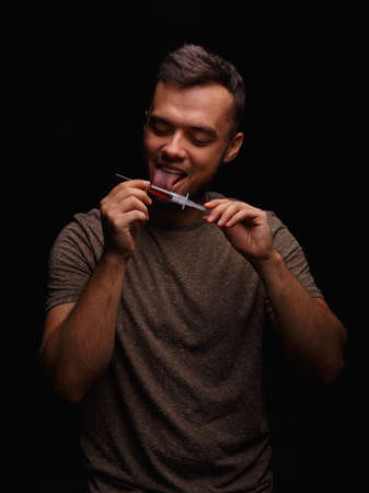 A guy with a drug obsession holds a syringe in his hand with an injectable drug in a dark black...