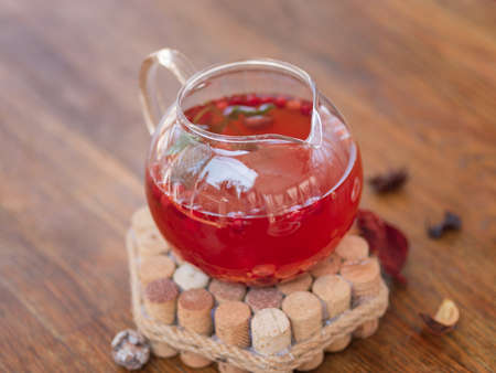 A big kettle of herbal black tea with strawberries, aromatic mint leaves and currant on a stand. Red...