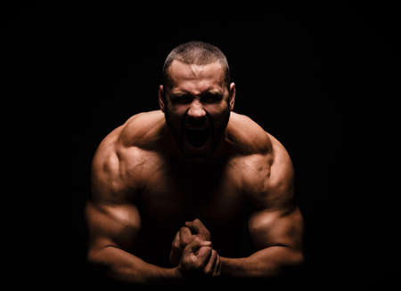 Close-up of a happy fitness model man with a muscular body on a black background. A Strong man with a biceps curl.の写真素材