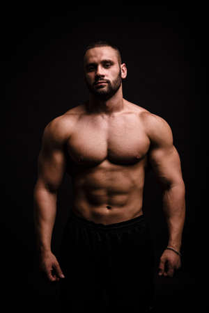 A portrait of a male with flexing muscles on a black background. Fitness training. A bodybuilder with a perfect body.の写真素材