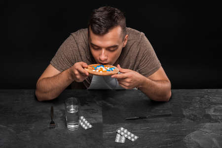 A hopeless junkie swallows drugs. A drug addicted sitting at the table on a black background. Drug concept. Copy space.の写真素材