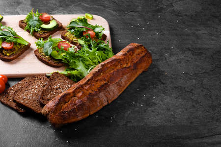 Close-up of a bread on a table background. A cut, crunchy dark baguette and a cutting desk with vegetable sandwiches.の写真素材
