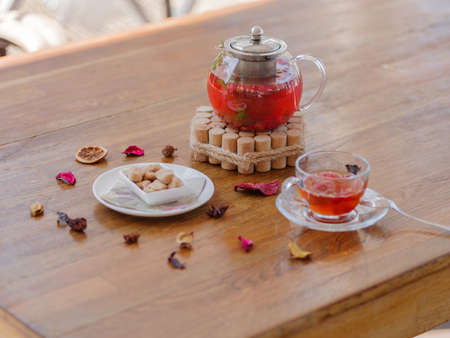 A bright berry tea in a glass teapot next to a transparent glass, a round white plate and dried fruits on a wooden background.の写真素材