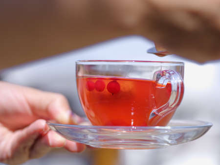A females hands with a cup of berries liquid on a blurred background. Delicious and natural strawberry tea.の写真素材