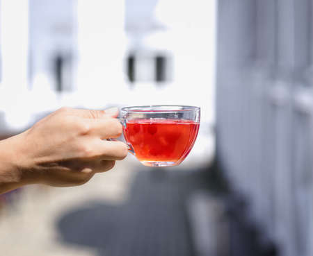 A ladys hand is holding a hot red drink from berries on a street blurred background. Fresh wild strawberry tea.の写真素材
