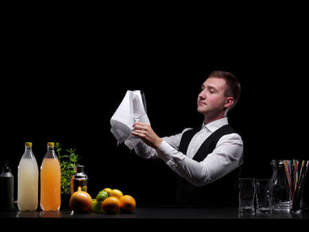 Bartender cleaning a glass. Barman and cocktail ingredients on a black background. Restaurant, club concept. Copy space.の写真素材