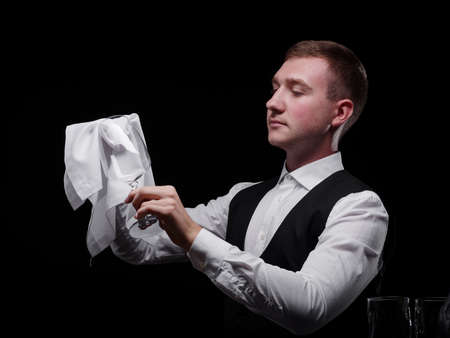 Bartender with a fancy glass. Barkeeper swiping a glass with a fabric on a black background. Restaurant service concept.の写真素材