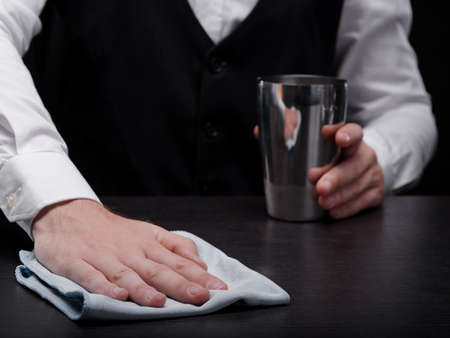Close-up of a bartender cleaning a bar counter. Barkeeper with a shaker and a white handkerchief on...