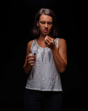 Woman taking antidepressants. A patient with pills on a black background. Stress, anxiety, depression treatment concept.の写真素材