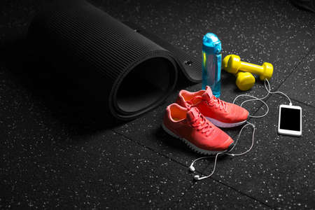 A view from above of a sportive bottle, bright pink training shoes, yellow dumbbells, pilates mat and smartphone on a black floor background. A colorful set of sportive accessories for gym training.の写真素材