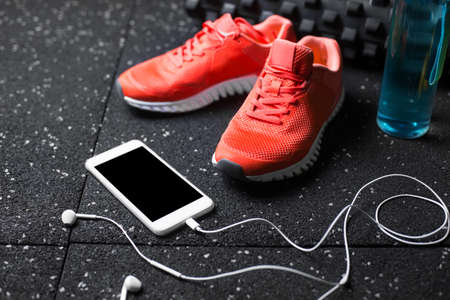 A composition of bright pink sports shoes, white smart phones, blue sportive shaker and pilates mat on a black background. A colorful composition of sportive accessories. Healthy lifestyle.の写真素材