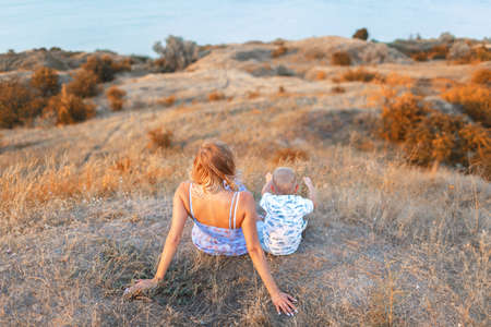 A little kid and his mother on a field background. A handsome family together enjoying a beautiful nature. Copy space.の写真素材