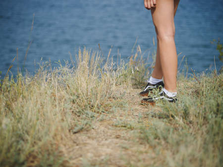 Close-up picture of fit, sporty woman's legs on a blurred natural background. A girl in snickers or suede shoes walking on a grassy hill. Camping, traveling, trip, journey concept. Copy space.の写真素材
