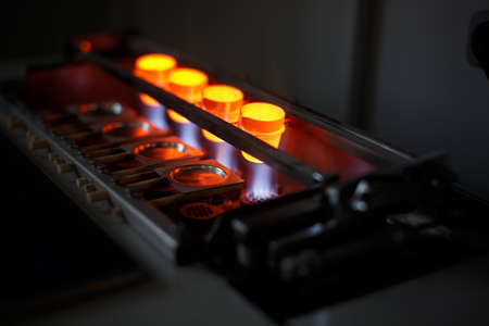 Close-up picture of a professional smelting gold machine in process. A bright red melting steel in little shaping forms on a blurred dark background. Metallurgical production of steel, bronze, metal.の写真素材