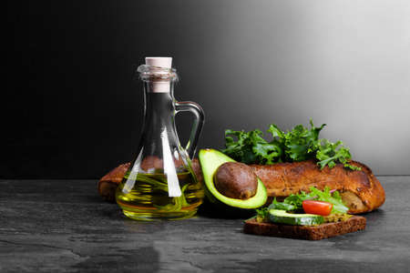A beautiful set of organic, rustic ingredients and a traditional avocado sandwich on a shiny stone background. Refreshing greens, olive oil, crusty bread and sauce in a bottle on a table. Copy space.の写真素材