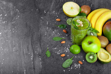A view from above of a freshly squeezed smoothie full of nutritious vitamins on a gray table background. A healthy composition from bananas, avocado, mint, cut kiwi and apple on a desk. Copy space.の写真素材
