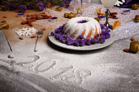 A beautiful Christmas composition from baked cake and organic coconut beverage on a gray background. A holiday's pie with icing and tender violet flowers. Cinnamon sticks and almonds on a table.の写真素材