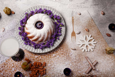 A top view of a composition of a traditional Christmas cake with icing and violet flowers around the baked dish on a plate and colorful background. A coconut beverage and a heap of almond on a desk.の写真素材