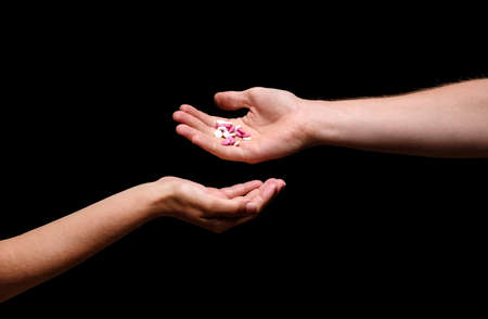 Close-up picture of a man giving different meds to a woman. Hands holding white and pink painkillers, antibiotics, drugs, vitamins or aspirin in round tablets on the black background.の写真素材
