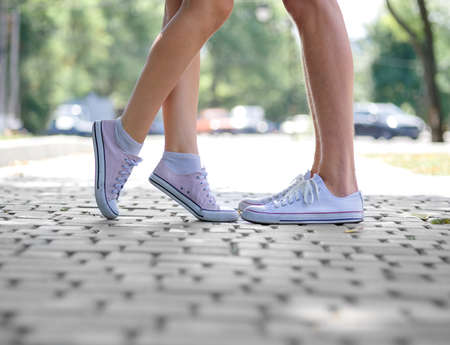 Modern urban hipster teenagers having fun. A close-up picture of teenages' legs in white and pink gumshoes on a blurred natural background. Teenagers kissing in park. Outdoors, romance, youth concept.の写真素材