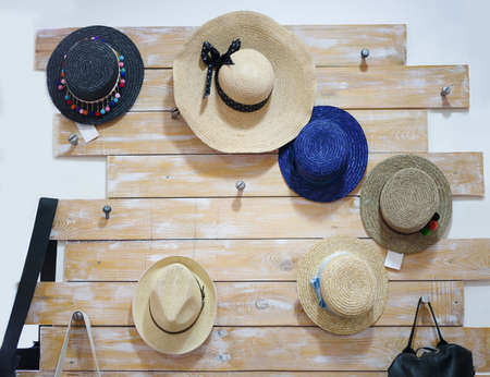 Classic, vintage women straw hats hanging on a wooden decorative desk on the white wall background. A composition of summer head accessories in a shop. Blue, beige, black classy panamas.の写真素材