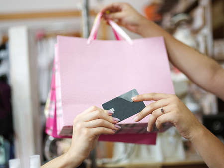 A close-up picture of colorful purchases and a credit card in female hands on a blurred background. A female paying by a credit card for her purchases in a clothing store. Shopping, money concept.の写真素材