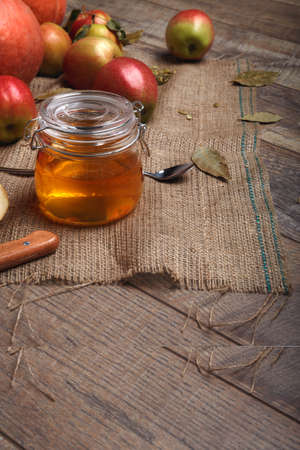A close-up picture of a colorful composition. Bright autumn fruits next to a glass jar of honey on a wooden table background. A pile of colorful apples next to a spoon and a knife on a rustic napkin.の写真素材