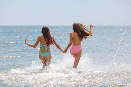 Stunning and good-looking ladies wearing colorful swimwears splashing in a blue sea on a sunny sky background. Happy, handsome teenage girls having a good time for summer vacation. Copy space.の写真素材
