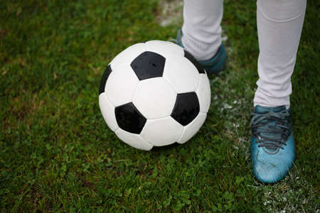 A view from above of a single soccer ball and guy's feet in sport's shoes on a bright green grass background. A round black and white football ball on a green field. Outdoors activities. Copy space.の写真素材