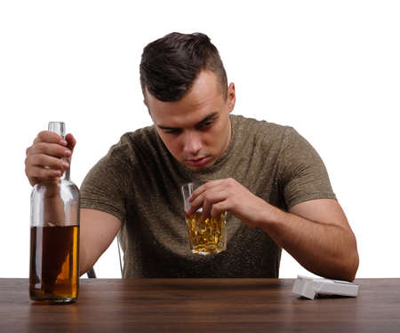 A young drunk man isolated on a white background. An alcoholic with a bottle of whiskey sitting at...