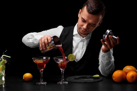 An attractive bartender pours a cocktail in a margarita glass, oranges, lemon, slices of lime on a black background.の写真素材