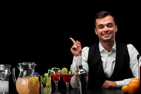 A bartender pointing at something, a bar counter with oranges, lemon, a shaker, margarita glasses on...