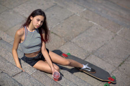 A beautiful girl with a longboard walks in a park on a natural blurred background.の写真素材