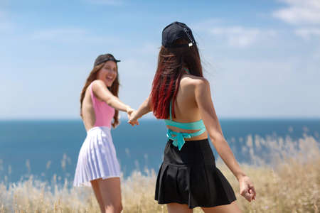 Two pretty girls smiling holding hands while walking on a seashore on a blurred natural background.の写真素材