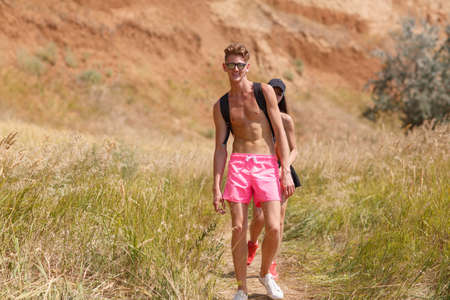 A full-length portrait of an attractive fellow in pink shorts strolling on a field on a blurred...