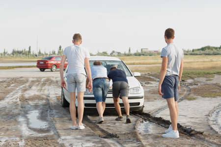 Four men pushing a car to pull it out of the mud on a road in the countryside on a natural blurred background.の写真素材