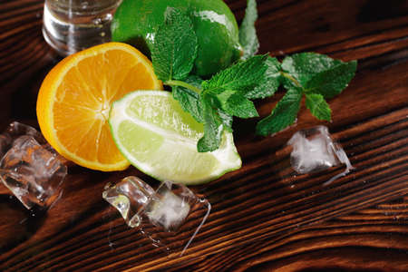 Close-up picture of a cut in half orange with a juicy texture and a slice of a sour, green lime on a wooden rustic background. Mint leaves and ice for a cocktail decoration. Refreshing summer fruits.の写真素材