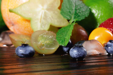 Closeup of yellow carambola, juicy grapes, fresh green leaves of pepper mint, red vivid strawberries, bright oranges, cool cubes of ice on a blurred colorful background.の写真素材