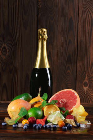 A table with bright grapefruit, carambola, blueberries, strawberries, oranges, fresh green leaves of mint, physalis, cubes of ice, grapes on a wooden brown background.の写真素材