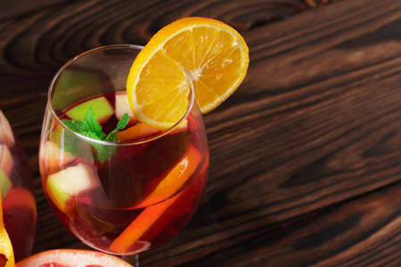 Closeup of a glass of a beverage with strawberries and pieces of apple and a leave of mint on a wooden background.の写真素材