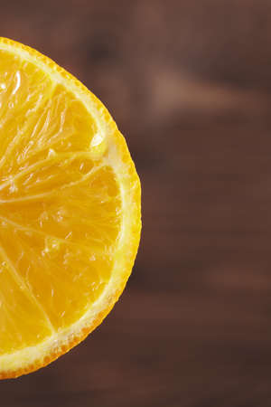 Closeup of a bright juicy succulent piece of an orange, fresh fruits for beverages on a brown blurred background.の写真素材