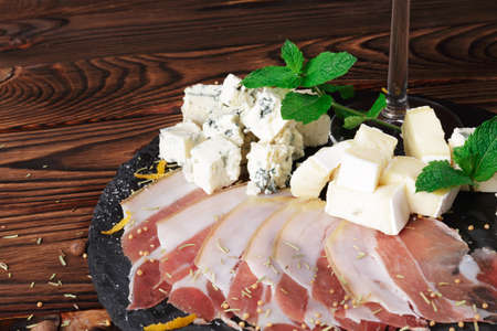 Closeup of a plate of Roquefort with distinctive veins of blue mold and prosciutto on a wooden background.の写真素材