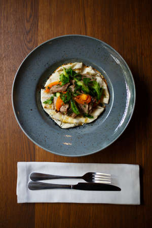 A top view of a delicious dish in a blue plate next to a dinner set on a dark wooden table background. Copy space.の写真素材