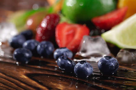 Close-up fresh, healthy, seasonal berries. Blueberries and red cut strawberry with lime fruit on a wooden background.の写真素材