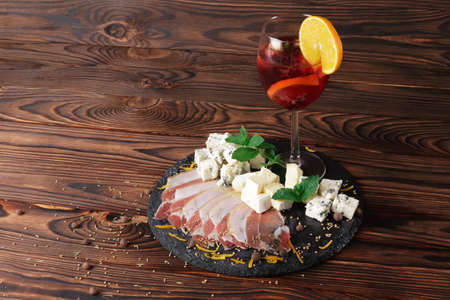 A wooden table with a plate of shhep milk blue cheese Roquefort and thinly sliced prosciutto with...